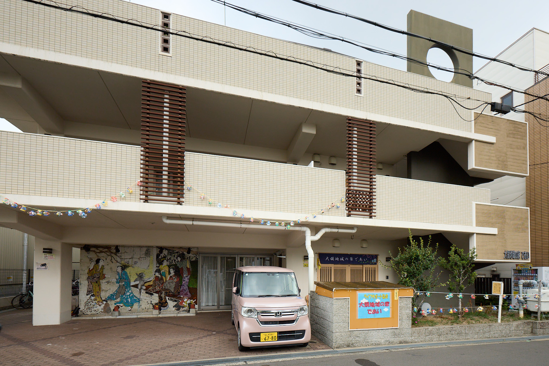介護施設の建物外観。白いタイル貼りの2階建て、駐車スペース付き