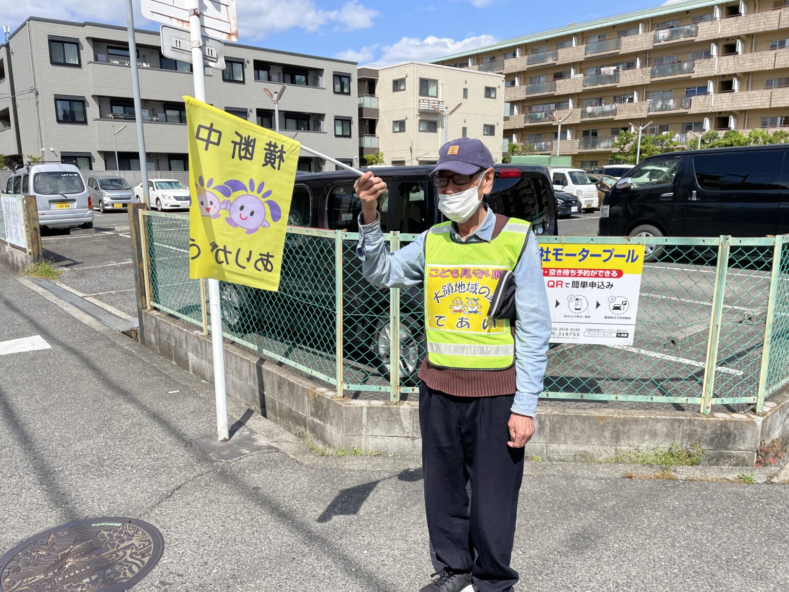 駐車場で黄色い看板を持つスタッフ。施設の交通安全啓発活動